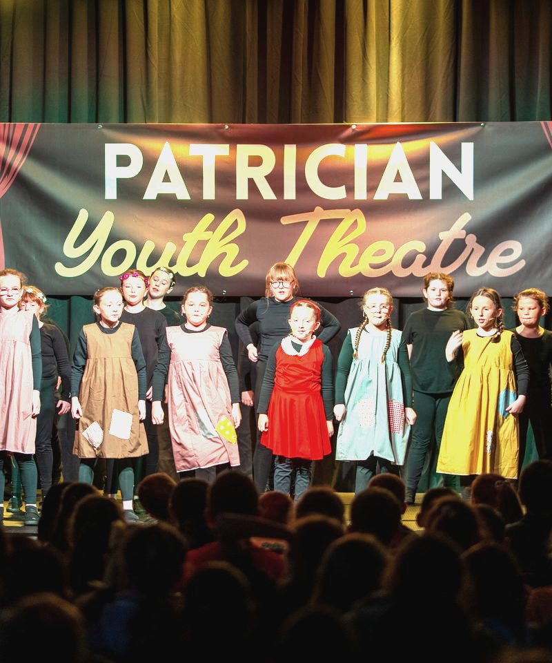 The Patrician Youth Theatre cast on stage under the company banner